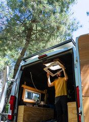 Handyman installing camper van roof window in pine forest