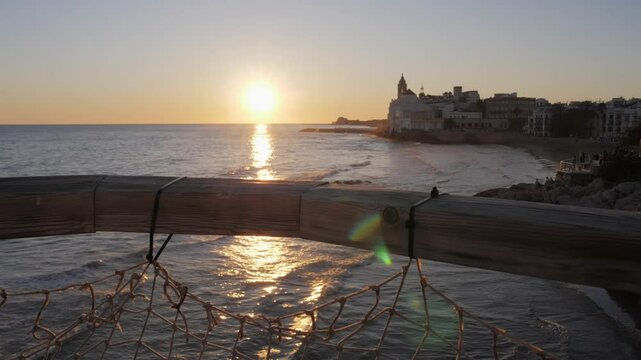 Beautiful sunset in seaside medieval Sitges city. Church of Sant Bartolomeu i Santa Tecla. Golden hour colours. Sun reflecting on the buildings. 