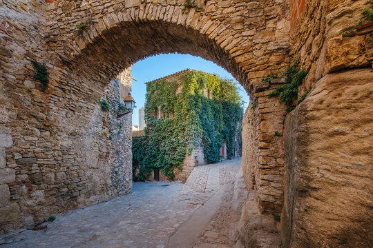 Medieval Archway Framing an Ivy-Covered Building. Scenic Street in Peratallada, Spain - Medieval Village in the Emporda - Powered by Adobe