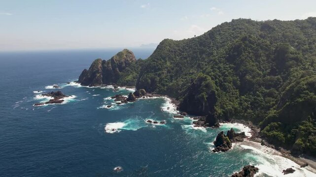 4K drone video of Orong Bukal Viewpoint. The blue Indian ocean crashes against cliffs and lush green landscapes amongst the mountains in Lombok, Indonesia