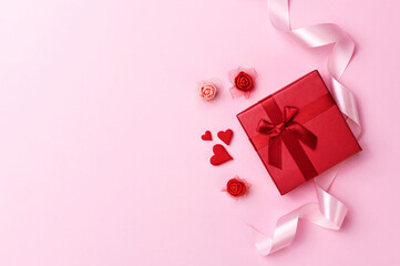 Red gift, rose flowers and small red hearts on pink background. Happy Valentines day, Mothers day, birthday, wedding concept. Romantic flat lay.