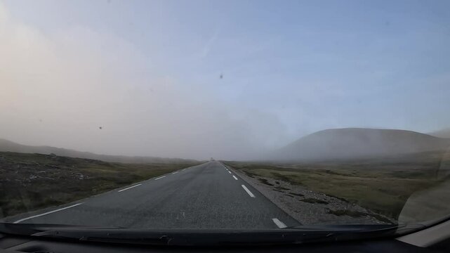 Driving through the tundra in northern Norway on E69 road. Surrounded by rocks and low grass. Foggy atmosphere creates a mysterious and serene landscape.