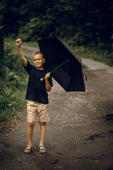 Happy boy standing under an umbrella during light rain