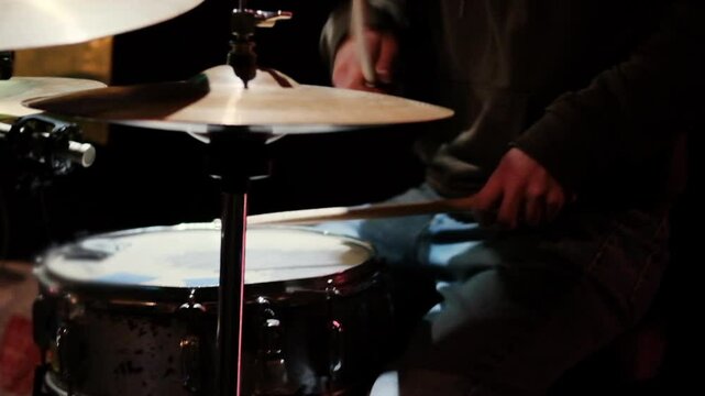 A drummer plays a snare drum and hi-hat cymbals during a live jam session, captured in low lighting for an intimate and artistic feel