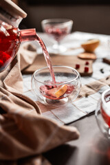 drops of red tea, woman pouring tea into a glass cup, hibiscus, tea with red berries, vitamin drink, winter tea for colds, lemon, red currant, black currant, raspberry, honey, cinnamon, anise