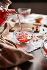 drops of red tea, woman pouring tea into a glass cup, hibiscus, tea with red berries, vitamin drink, winter tea for colds, lemon, red currant, black currant, raspberry, honey, cinnamon, anise
