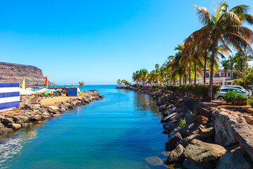 Picturesque coastal scene of Puerto de Mogan from Gran Canaria, narrow waterway flanked by rocky embankments leading to ocean