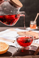 drops of red tea, woman pouring tea into a glass cup, hibiscus, tea with red berries, vitamin drink, winter tea for colds, lemon, red currant, black currant, raspberry, honey, cinnamon, anise