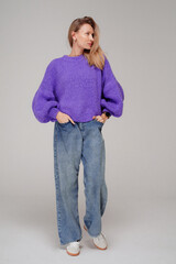 Trendy, fashionable woman posing in warm sweater and wide jeans, studio background
