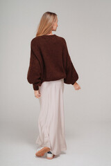 Back view of trendy, fashionable woman posing in warm sweater, maxi skirt and sporty shoes, studio background.