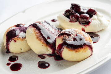 A delicious plate of sweet cheese dumplings drizzled with berry sauce, topped with whipped cream and fresh berries. Perfect for dessert lovers or brunch enthusiasts.