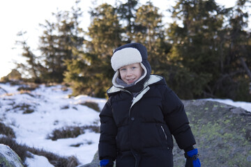 Portrait of a boy in winter outerwear against the backdrop of a snow-covered meadow and forest