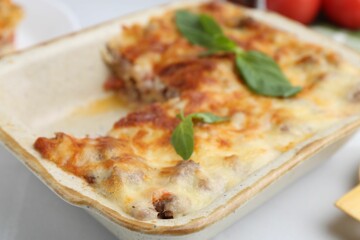 Delicious cooked lasagna with basil in baking dish on white table, closeup