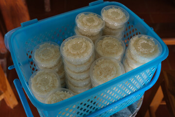 Khao Mak in plastic cup. Khao Mak is a type of Thai dessert, It is made from steaming glutinous rice and then fermenting it with mold and yeast in the form of flour in a blue basket.
