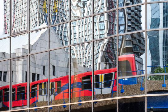 The vibrant colors of a rail transit visible in reflective glass towers, capturing the dynamic interaction between urban architecture and public transportation in London UK