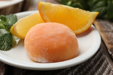 Plate with tasty mochi, cut orange and mint on wooden table, closeup