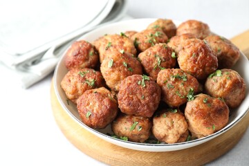 Tasty cooked meatballs with green onion in bowl on white table, closeup