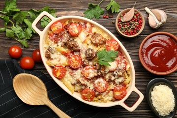 Delicious pasta casserole with cheese, tomatoes and minced meat in baking dish served on wooden table, flat lay