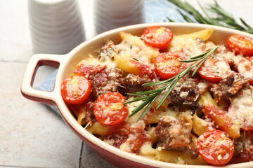 Delicious pasta casserole with cheese, tomatoes, minced meat and rosemary in baking dish on tiled table, closeup