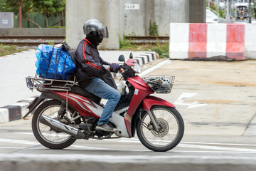 Fototapeta premium A man rides a motorcycle with a load down the street, Bangkok, Thailand