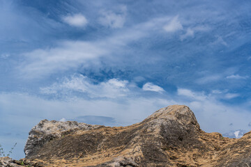 A rocky outcrop sits beneath a blue sky with wispy clouds, showcasing natural textures and colors.