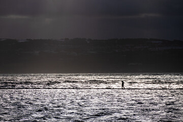 Single person in silhouette walking around coastal marine lake in dark and stormy weather conditions