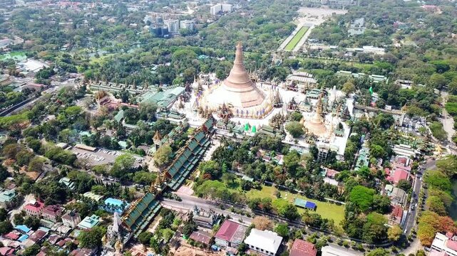 A stunning aerial view of the Shwedagon Pagoda surrounded by lush greenery in Rangun, Myanmar, showcasing its golden spire and intricate architecture in the heart of the city