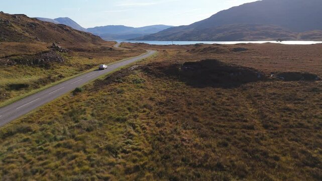 An electric car driving on North coast 500 on a sunny day with view of lake Assynt in Scotland