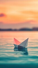 A delicate paper boat floats effortlessly on the smooth surface of the ocean as the sun sets, casting a warm glow on the tranquil water