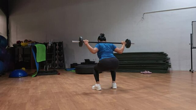 fitness, exercise, weight lifting and healthy lifestyle concept, back view of 40 year old sporty woman exercising with barbells in the gym