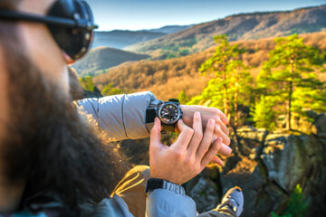 Male hiker checking time on wristwatch while resting on a mountain summit during autumn. Scenic...