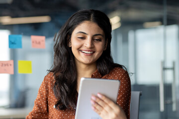 Businesswoman using tablet computer at work inside office. Smiling woman using app and reading...