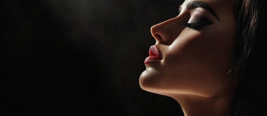 Stunning profile of a young brunette woman with elegant makeup and dramatic lighting, isolated on a dark background emphasizing beauty and serenity