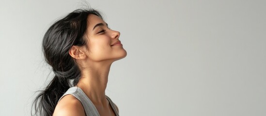 Young Hispanic woman in casual sleeveless shirt relaxing in profile pose with confident smile and natural expression against light gray background.