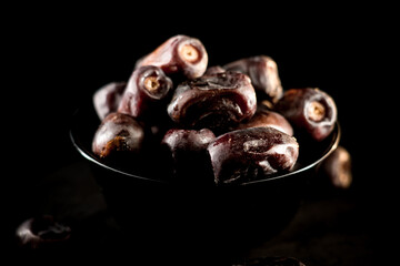 Dried dates served in a sleek black bowl against a dark background showcasing rich textures and alluring details