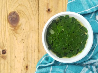 Moringa leaves soup in bowl on wooden table. Top view angle setup with negative space 