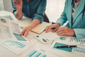 Two Asian women are reviewing financial transaction documents and calculating expenses with a...