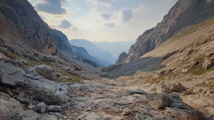 A rocky valley surrounded by towering mountains under a cloudy sky.