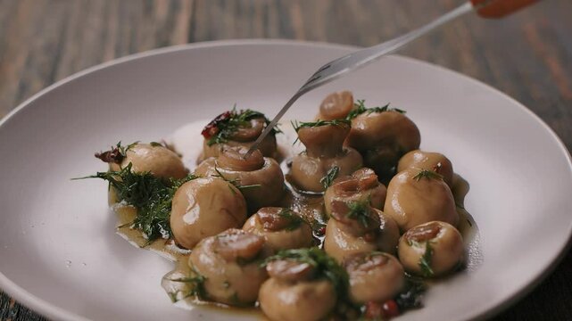 A fork spears and lifts marinated champignons from a plate. Close-up. High quality 4k footage