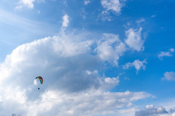 A paraglider floats gently through a blue sky filled with fluffy white clouds, a sense of freedom.
