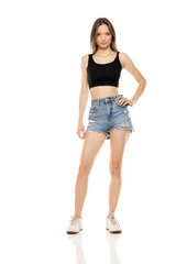 Beautiful young woman in a short blue jeans and black sleeveless shirt on a white studio...
