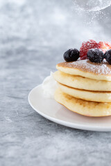 粉砂糖が振りかけられてベリーがトッピングされ積み重ねられたパンケーキ