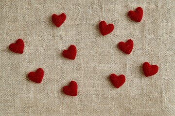 Fototapeta premium Nine red felt hearts scattered on beige linen fabric.