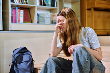 Upset sad teenage girl high school student sitting on floor in library classroom