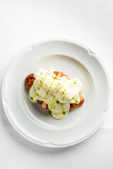 A delicious croissant topped with creamy hollandaise sauce and garnished with green onions on a white plate. Perfect for a gourmet breakfast or brunch setting.