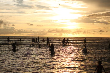 Fototapeta premium Silhouette people man a woman on the sunset background, mSunset on the tropical beach Seminyak. The tourists watching for beautiful sunset in the sea. Coast of the sea at colorful sunset.