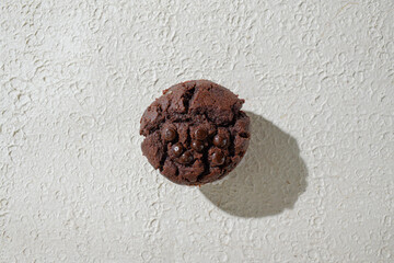 A chocolate topped with chocochips, set against a textured white background for a clean and appealing look
