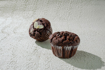 Two of cupcakes on textured white: one chocolate with chocochips and one chocolate with almond...