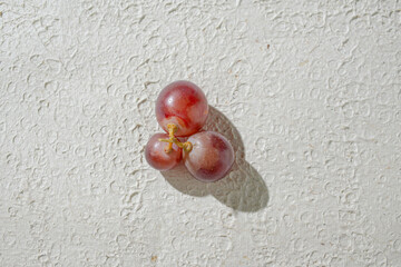 Close up of vibrant red grapes against a textured white background, highlighting their freshness and texture