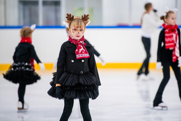 Little girl in reindeer costume skating on ice rink, children's sports festival.